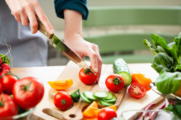Beautiful young woman slicing red ripe tomato, preparing delicious fresh vitamin salad. Concept of clean eating, healthy food, low calories meal, dieting, self caring lifestyle. Close up
