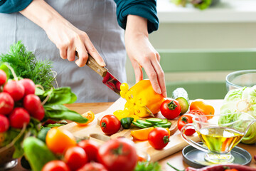 Beautiful young woman slicing yellow pepper, preparing delicious fresh vitamin salad. Concept of clean eating, healthy food, low calories meal, dieting, self caring lifestyle. Close up