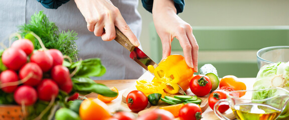 Beautiful young woman slicing yellow pepper, preparing delicious fresh vitamin salad. Concept of clean eating, healthy food, low calories meal, dieting, self caring lifestyle. Close up