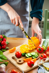 Beautiful young woman slicing yellow pepper, preparing delicious fresh vitamin salad. Concept of clean eating, healthy food, low calories meal, dieting, self caring lifestyle. Close up