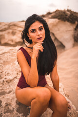 Caucasian brunette in a maroon swimsuit, sitting on the beach of Cabo de Gata, Nijar. Andalucia, Spain