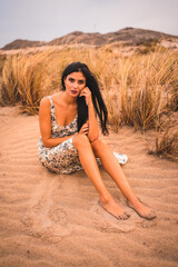 Caucasian brunette in a white floral dress, sitting on the beach of Cabo de Gata, Nijar. Andalucia, Spain