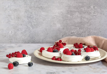 Fresh baking meringues or mini Pavlova on the plate. Sweet dessert decorated with different berries. 