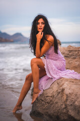 Fototapeta na wymiar A young brunette Caucasian in a pink cloth dress, on the beach by the sea in Cabo de Gata, Nijar. Andalucia in Spain