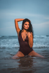 Fototapeta na wymiar Caucasian brunette in maroon swimsuit, on the beach enjoying the holidays in the sea water on her knees