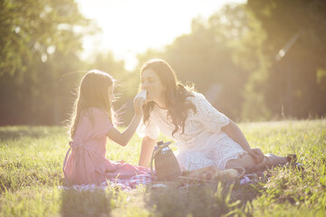 Mother and daughter sitting in nature and having picnic.