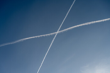 White trails, from jet exhaust, form a cross in the sky. A blue sky on the background