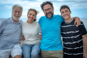 Smiling multigeneration family, sitting outdoors by the sea. From senior adult to teenager boy