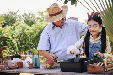 Asian retirement grandfather and pretty granddaughter helping prepare planting soil together for planting trees at home garden. Happy and enjoy family outdoor activity in holiday.