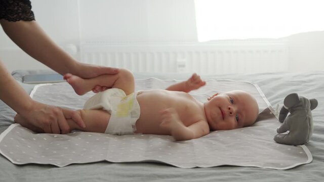 Mother with baby boy doing exercise simple exercises to make baby bones and muscles stronger, newborn infant lying on bed against the window. High quality 4k footage