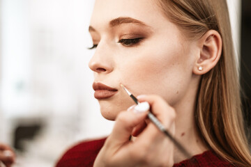 makeup artist paints lips with lipstick with a brush on a beautiful young woman blonde model, face make up concept