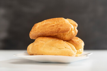Profiteroles on white plate. Close up. Homemade puffs, popovers and eclairs. Side view
