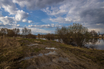On the horizon is a village by the river. A road with puddles and mud. Rural landscape in early spring.