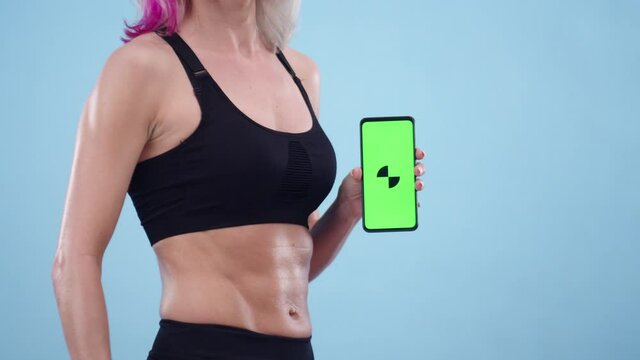 Woman in sports top and with a muscular stomach holds a phone with an app, close-up. Concept of apps and programs for sport.