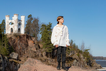 A boy standing on a granite rock against the background of a blue sky and a white castle