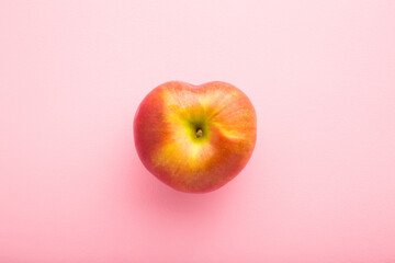 Heart shape of red apple on light pink table background. Fresh fruit. Pastel color. Closeup. Top down view.