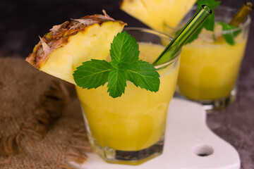 Two glasses of fresh pineapple smoothies on a gray background.