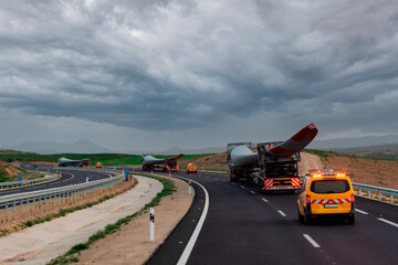 Special transport trucks with a wind turbine blade each circulating accompanied by signaling vehicles.