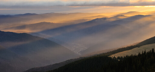 Golden morning rays over the mountain ridge and forest. Beautiful foggy morning in the mountains