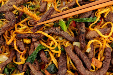 Beef and egg noodle stir fry with vegetables and wooden chopsticks background
