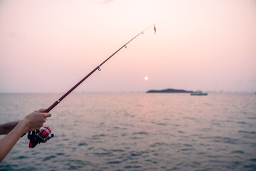 Woman hand holding fishing rod with sea background, fishing at sunset.