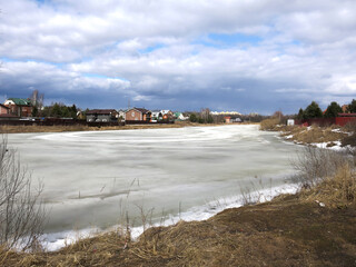 country pond, covered with a crust of spring ice with cozy houses in the distance