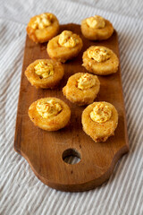 Homemade Deep-fried Deviled Eggs with Paprika on a rustic wooden board, low angle view.