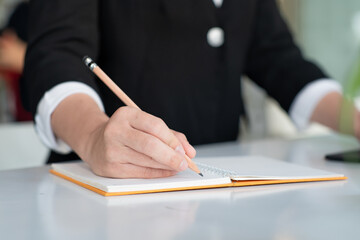 Closeup view of woman hand using pencil writing on note pad while sitting at the table.