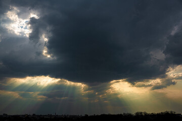 Dark sky with clouds, through which the rays of the sun break through