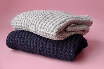 Stack of cozy knitted sweaters on pink background. Autumn-winter concept