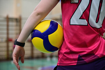 A volleyball player stands with her back to the camera holding a volleyball between her hand and body.
