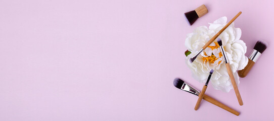 Top view of pink background and white peony, professional makeup brushes on it.Banner for ad