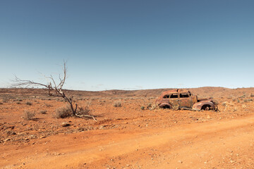 The rusted abandoned wreck of an old car in a remote area of Australian Outback on a rural dirt...