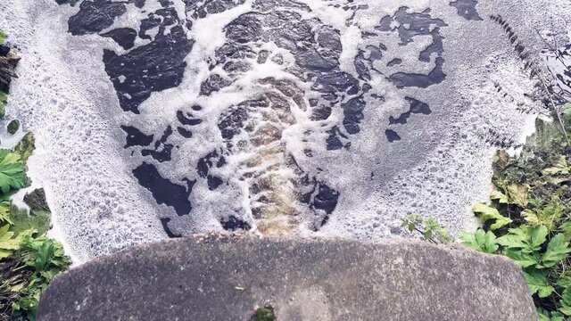Brown swamp water full of organic substances flows down the pipe and forms a plentiful foam, biofouling