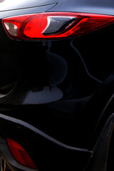 Fototapeta premium Black car with red headlight close-up, rear view, side view. An abstraction.
