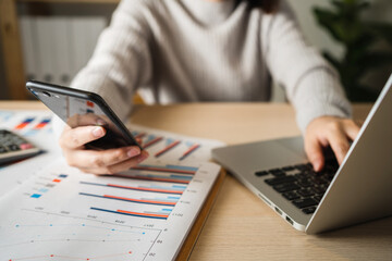 Fototapeta premium Businesswoman talking via smartphone and using laptop working analyzes business data at home, work from home concept.