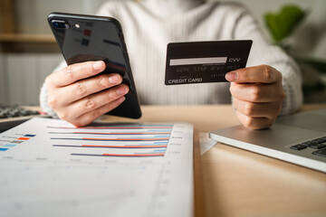 Businesswoman using smartphone shopping online via credit card while working analyzes business data at home, work from home and .e-commerce concept.