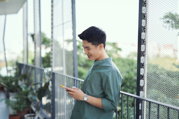 Young man standing on balcony texting on mobile phone,