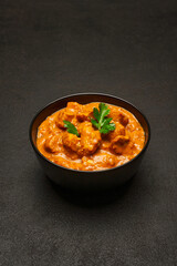 Black ceramic bowl of Traditional Chicken Curry on dark concrete background
