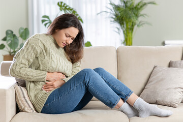 Young woman sitting on the couch at home with a pain in her stomach.