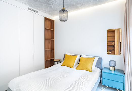 Clean bright bedroom with bed, duvet,side table, lamps,curtain, metal mirror, led indirect light and painted wallpaper on the ceiling. Minimalist white stylish interior with wood and brass details.
