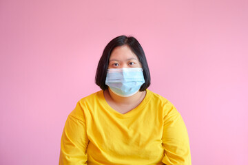 Image of a young woman with Down syndrome Wear a mask to protect against the COVID-19 coronavirus. She is a cerebral palsy student called Down syndrome. She wore a yellow dress on a pink background.