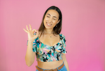 Young beautiful woman wearing casual shirt standing over pink isolated background smiling positive doing okay sign with hand and fingers. Successful expression.