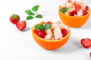 Fruit salad served in orange half. Orange, pear, apple, banana, strawberry, pine nut and mint chopped and mixed in the organic bowl