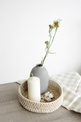 there is a candle in a round basket and a vase of flowers on the table. white background, room