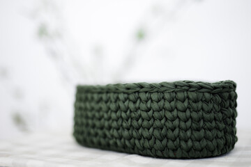 oval knitted basket of dark green color on a napkin in the room. flowers on the background