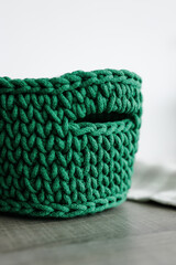 rectangular basket with green handles woven from knitwear on the table. white background