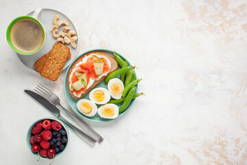 Healthy breakfast -  open sandwich with salmon and cucumber, boiled eggs, peas, coffee, biscuits, nuts and berries on a bright background. Top view. Copy space