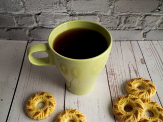 yellow mug with coffee, yellow cookies in the foreground, behind a white brick wall and a green plant