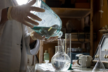 Scientist in a white coat and gloves conducts an experiment, he pours liquid from one flask to another, in the laboratory.